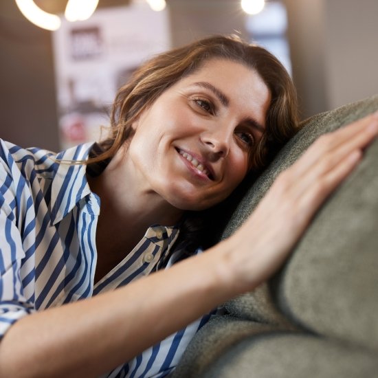Eine Frau mit braunen Haaren, lehnt mit dem Kopf an einem Polstermöbel und fährt mit der Hand über den grünen Stoff des Sofas