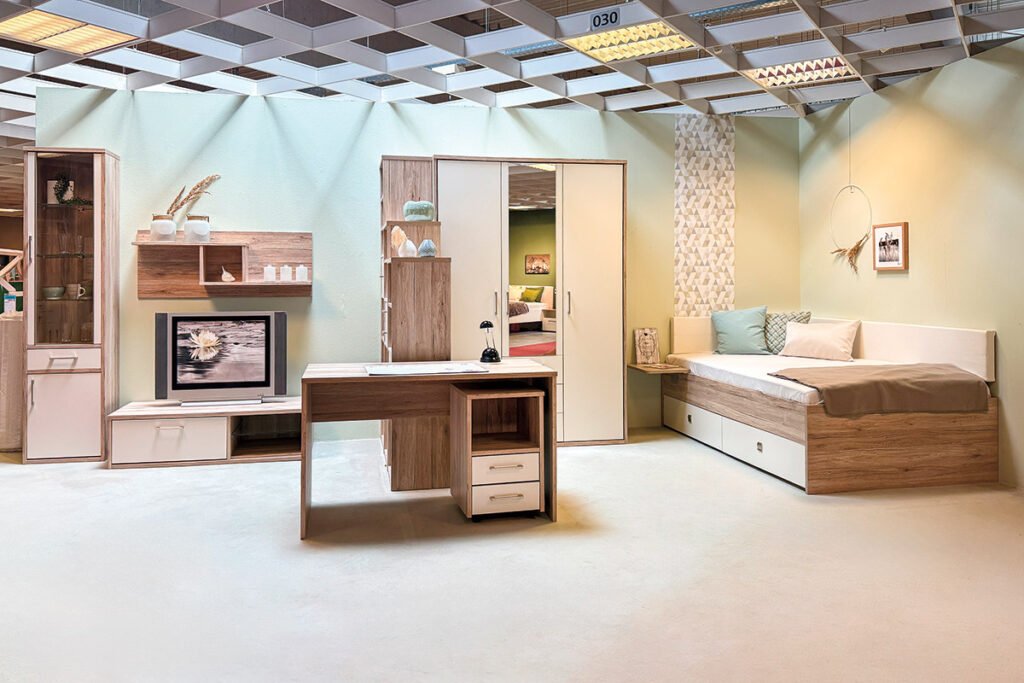 Jugendzimmer San Remo/Lichtweiß, bestehend aus von links Vitrine mit 4 Böden hinter Glastür, einer Schublade und einer Tür, Lowboard mit einer Schublade und einem offenen Fach, Wandpaneel, 3 Regalen in verschiedenen Höhen, Drehtüren-Kleiderschrank mit 3 Türen, davon eine mit Spiegel, Regalbrett am Bett, Bett, mit Kopfteilpolster und seitlichem Polster, sowie 2 Schubladen unter der Liegefläche, Schreibtisch und Rollcontainer mit zwei Schubladen und einem offenen Fach oben