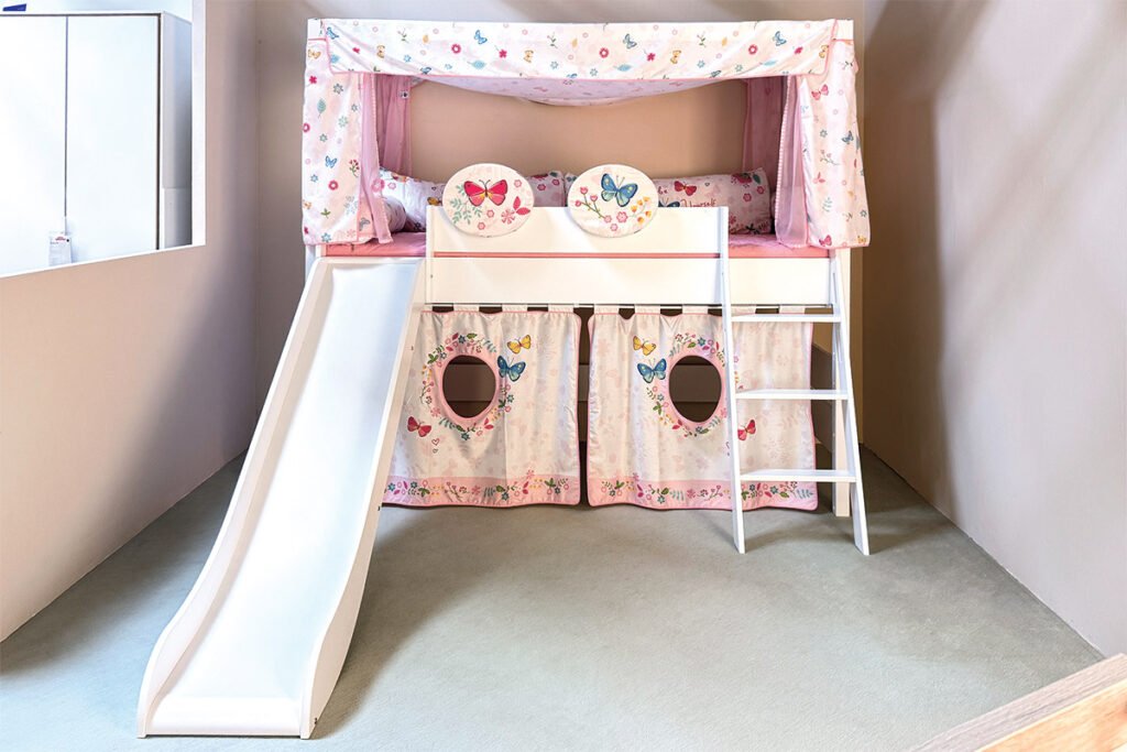 Hochbett Weiß mit Baldachin, Kissen und Vorhang in Rosa mit Schmetterlingen, links befindet sich eine Rutsche und rechts eine Leiter