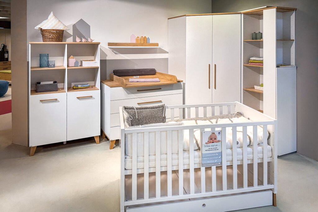 Babyzimmer Weiß/Eiche Nebraska Nachbildung, bestehend aus Standregal mit 4 offenen Fächern und zwei Türen, Wandregal, Wickelkommode mit 4 Schubladen, Eck-Kleiderschrank mit 2 Türen und Regalmit 6 Böden und einer Tür sowie Babybett