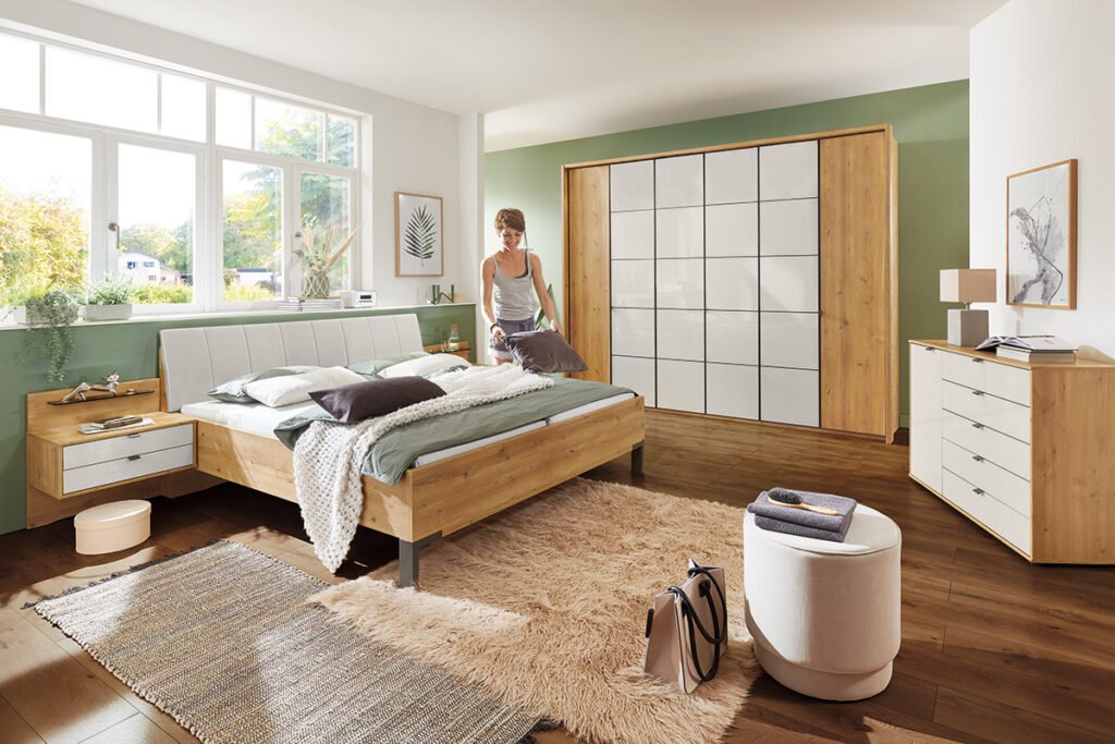 Schlafzimmer mit Bettanlage, Nachkonsolen, Drehtürenkleiderschrank und Kommode in Bianco-Eiche Nachbildung und Absetzungen in Glas Champagner