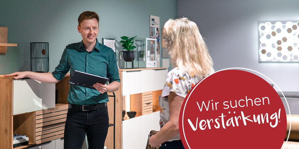 Beratungssituation mit Verkäufer und Kundin, auf dem Foto ist ein Button mit dem Spruch "Wir suchen Verstärkung"