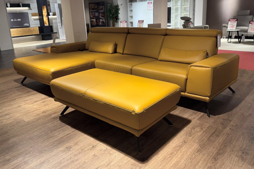 Ecksofa Leder Senfgelb, Füße Schwarz, mit Hocker und zwei Nierenkissen.