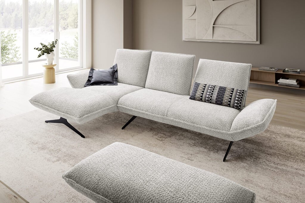 Ecksofa mit Stoffbezug in Hellgrau und Metallkufen, dazu ein Hocker